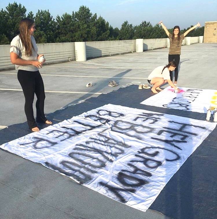 Banner Event: Spirit Club members put a lot of work in before all the shouting at games take place. Shown here painting a banner on the parking deck are juniors Chloe Van Nort and Annabel Santoli along with senior Addie Derrick.